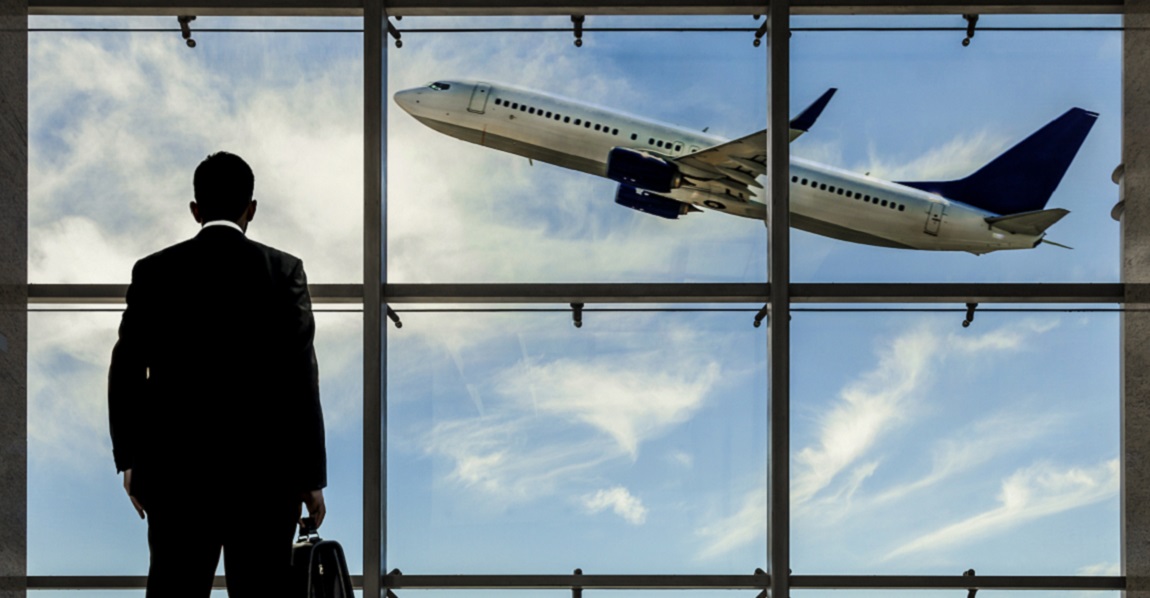 Businessman in airport looking on airplane in sky